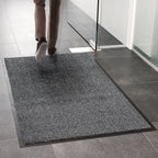 Person stepping onto a gray doormat in a tiled room.
