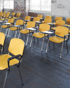 Yellow chairs with black armrests arranged in a classroom setting.