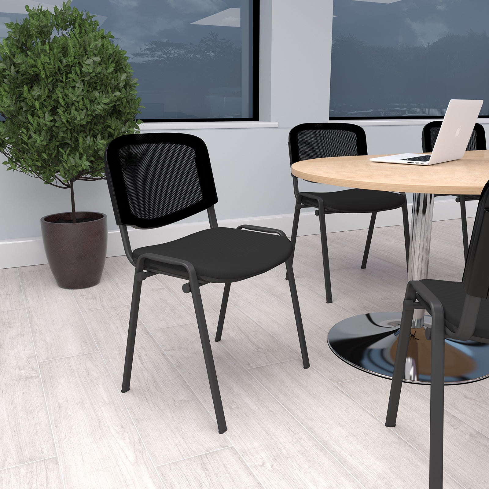 Black chairs around a wooden table in an office setting with a plant and wall art.