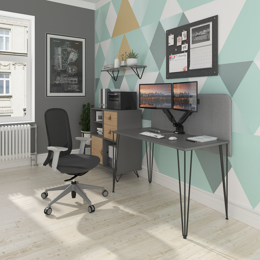 Modern home office setup with a compact desk featuring black hairpin legs, dual monitors on an adjustable arm, an ergonomic office chair, storage cabinet, and geometric patterned accent wall.