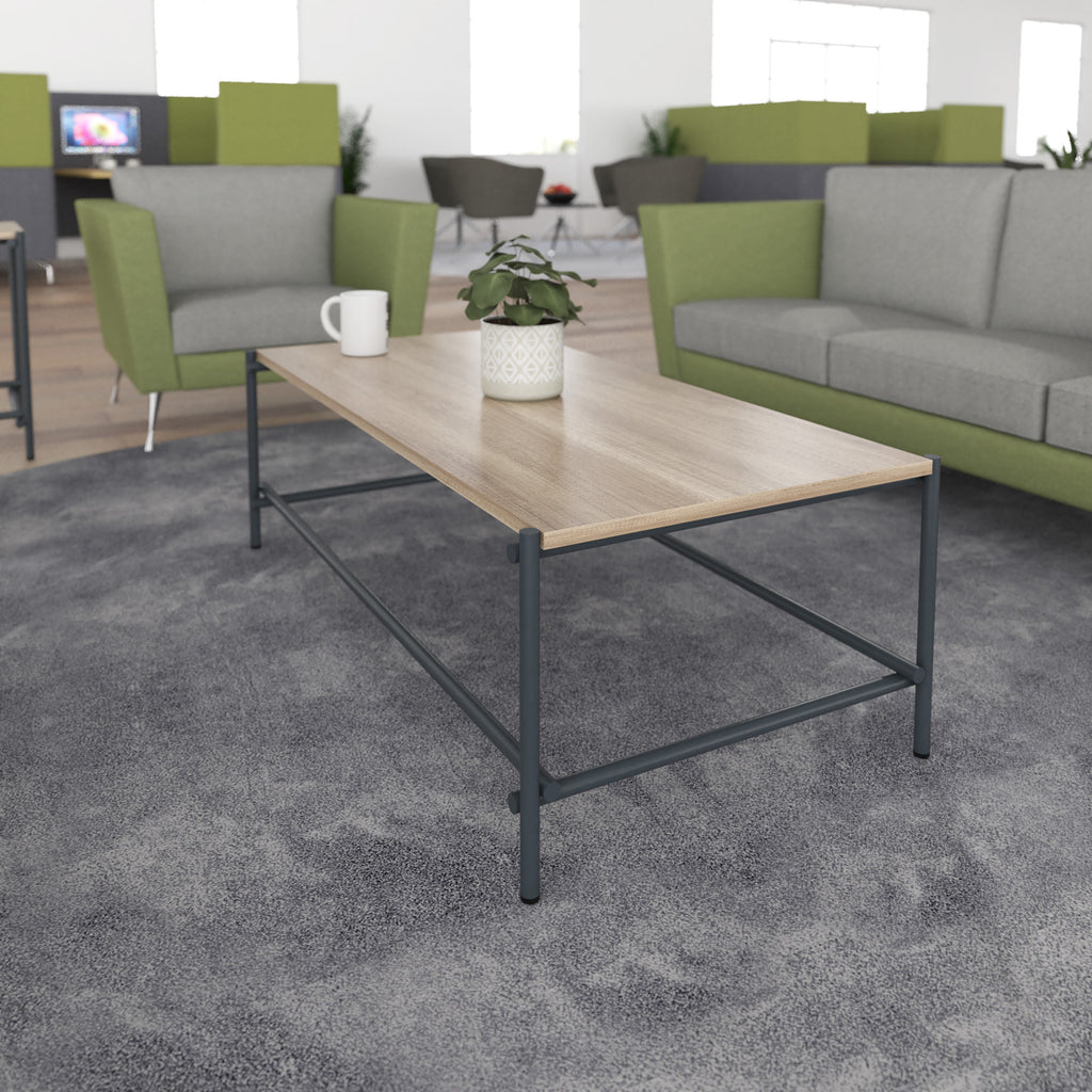 Rectangular coffee table with a wood-effect top and black metal frame, shown in a modern office lounge with green and grey seating.