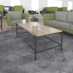 Rectangular coffee table with a wood-effect top and black metal frame, shown in a modern office lounge with green and grey seating.
