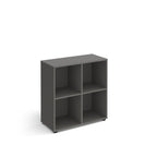 Grey office storage unit with four open cubby compartments, rectangular design, and small adjustable feet, shown on a white background.