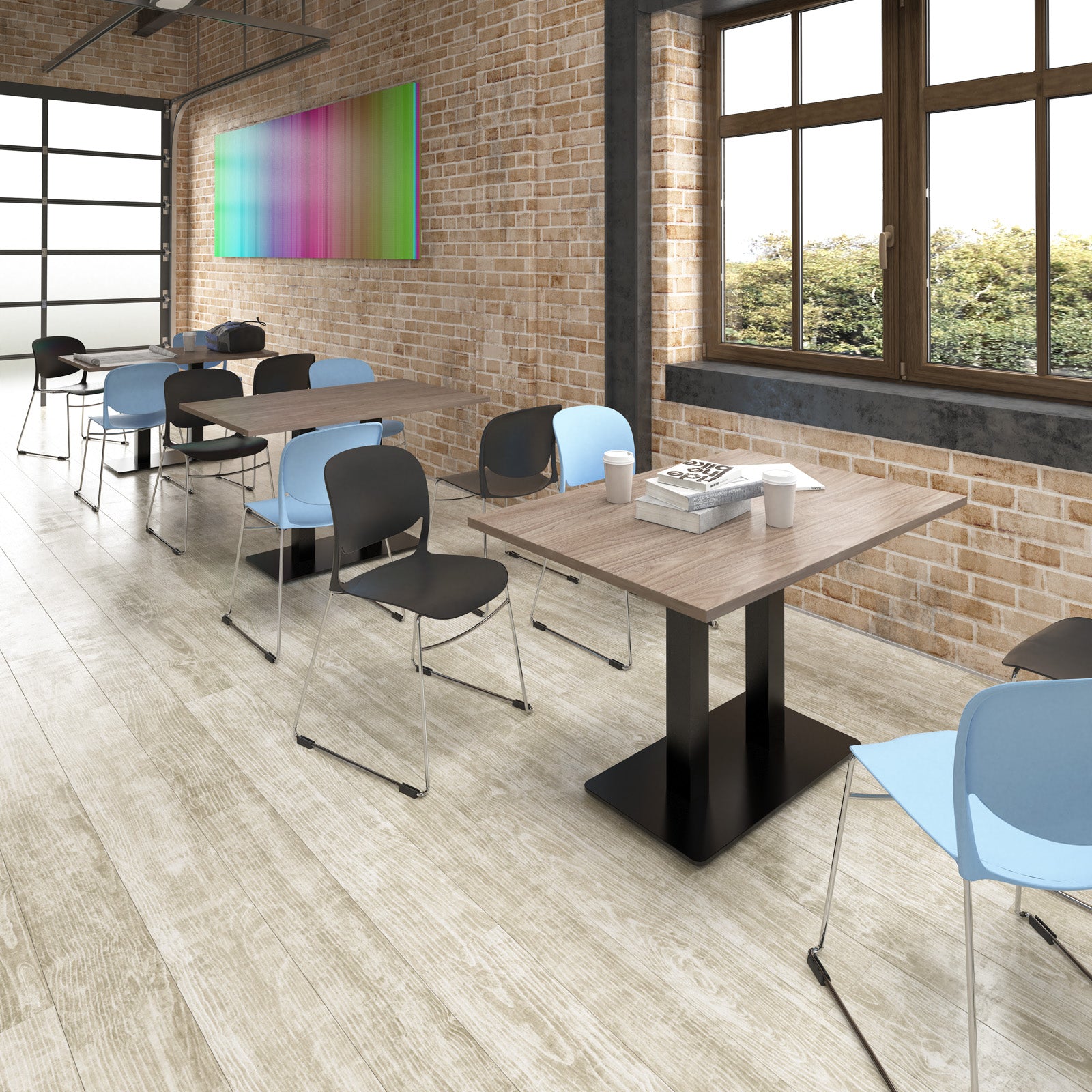 A modern classroom or meeting space with light wood tables, black and light blue chairs, brick walls, large windows, and a colorful abstract wall art piece.
