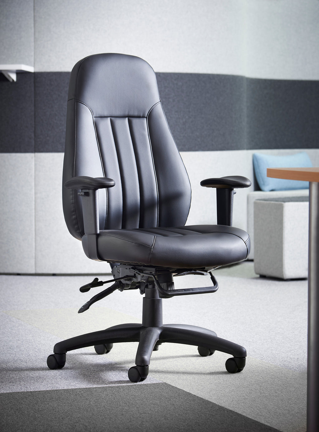 Black leather executive office chair with padded high back, adjustable armrests, and a five-star wheeled base, shown in a modern office environment.